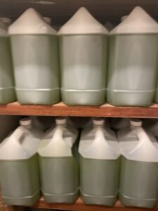 Row of green plastic jugs with pour spouts on a wooden shelf